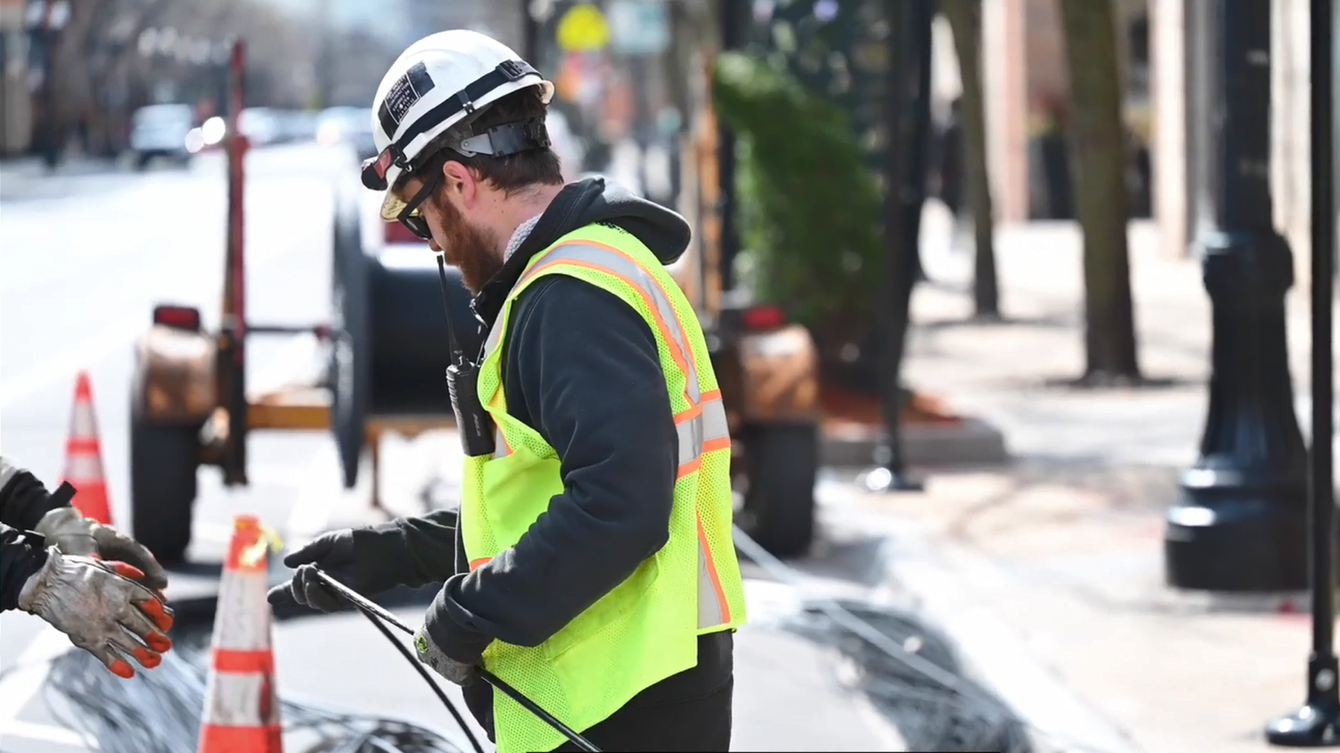 A person in high visibility vest working with fiber deployment in the street.