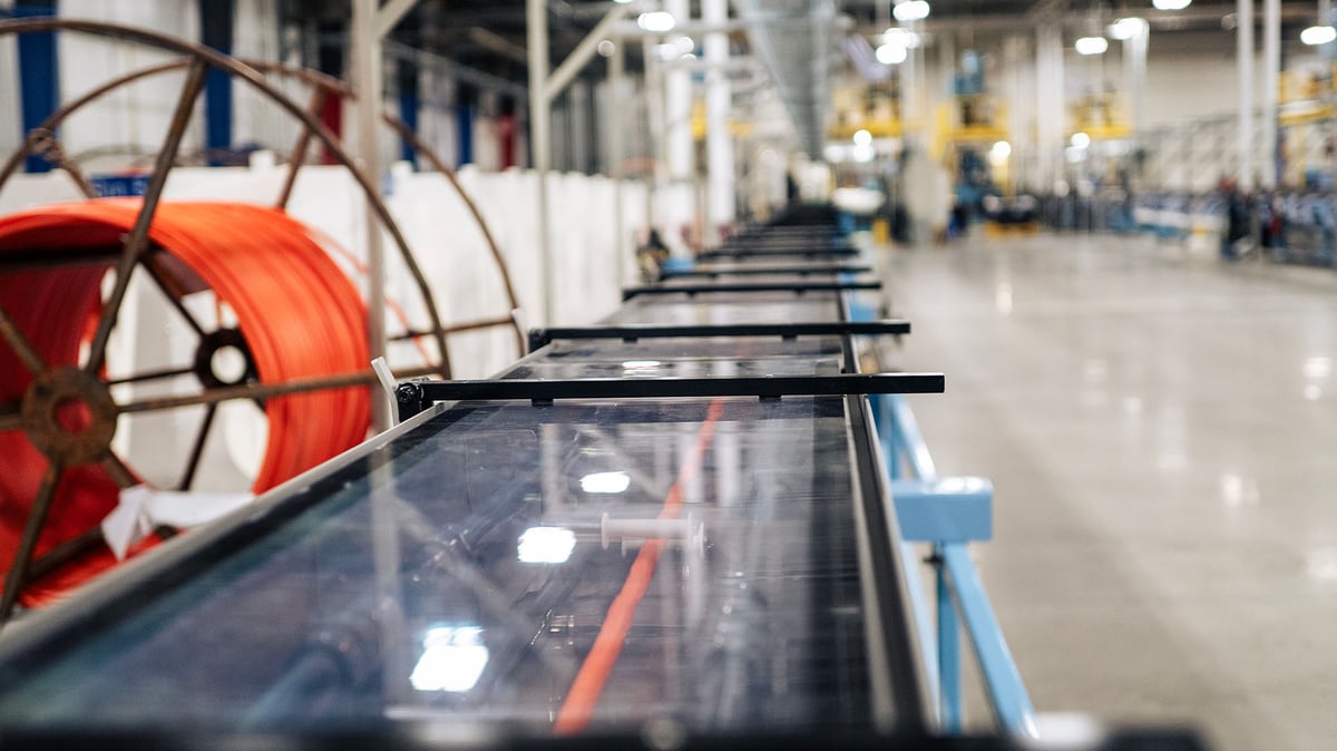 A production line producing microduct in a well-lit factory hall. You can see an orange microduct in the cooling bath.