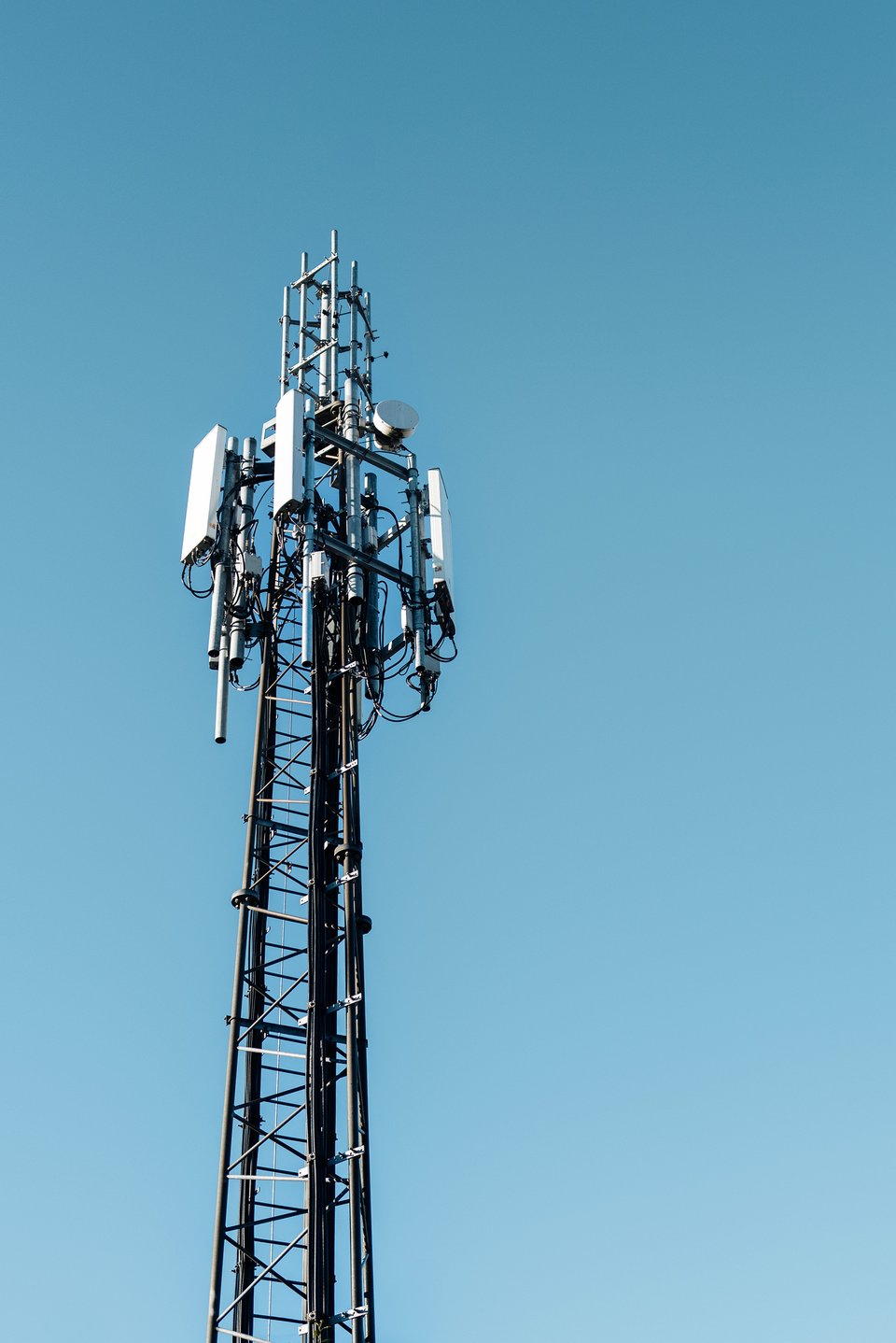 A tall metal tower with antennas and communication equipment on top. It is a cell tower that helps maintain cellular networks. The sky is clear.