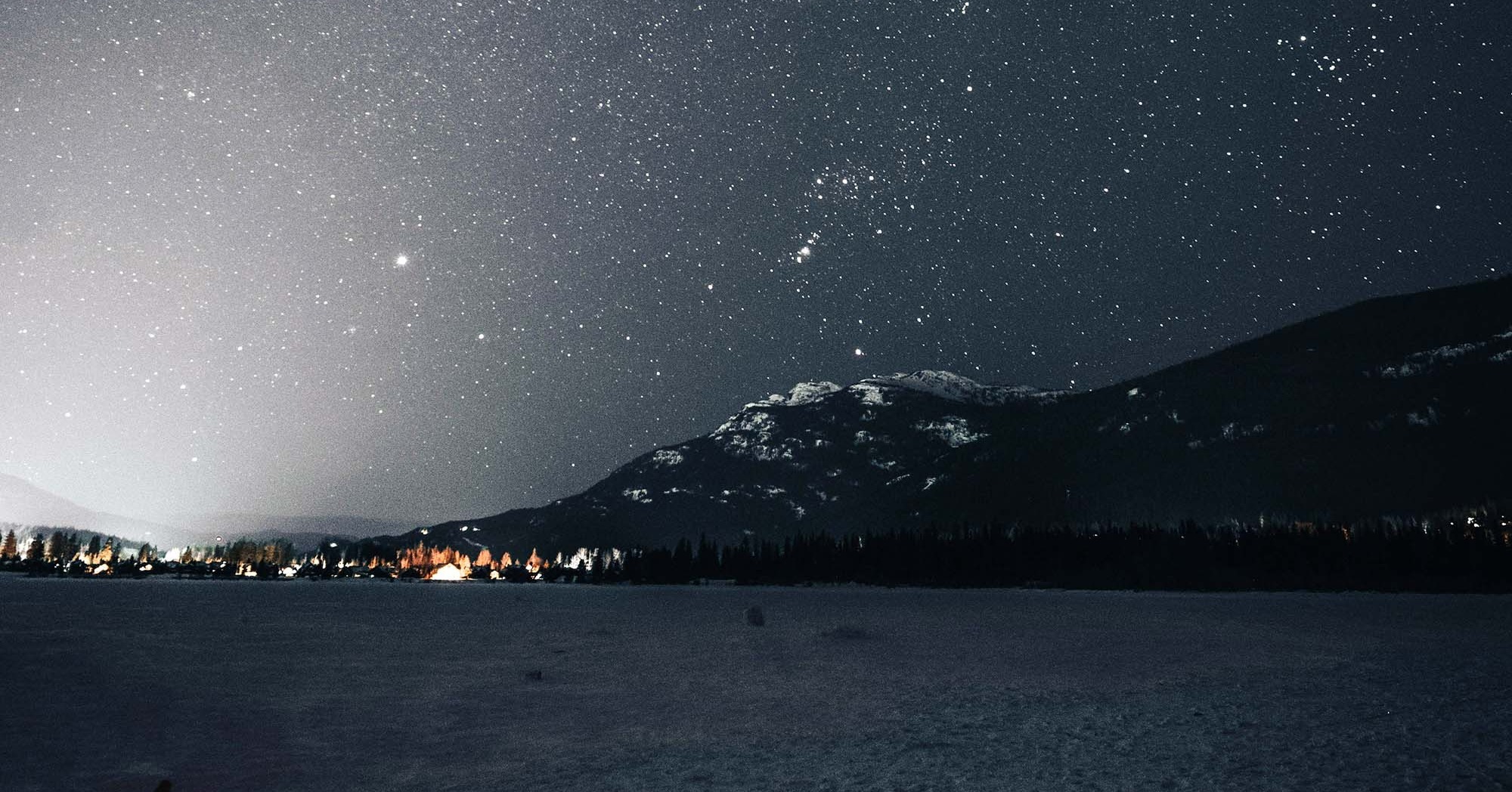 Snowy, winter landscape at night under the stars. A village amongst mountains.