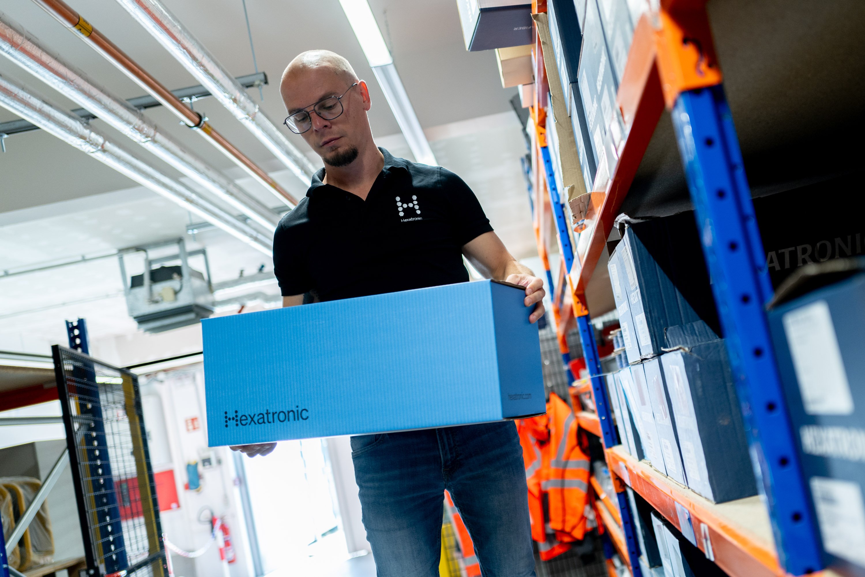 A person holding a blue Hexatronic Stingray box in a warehouse storage area.
