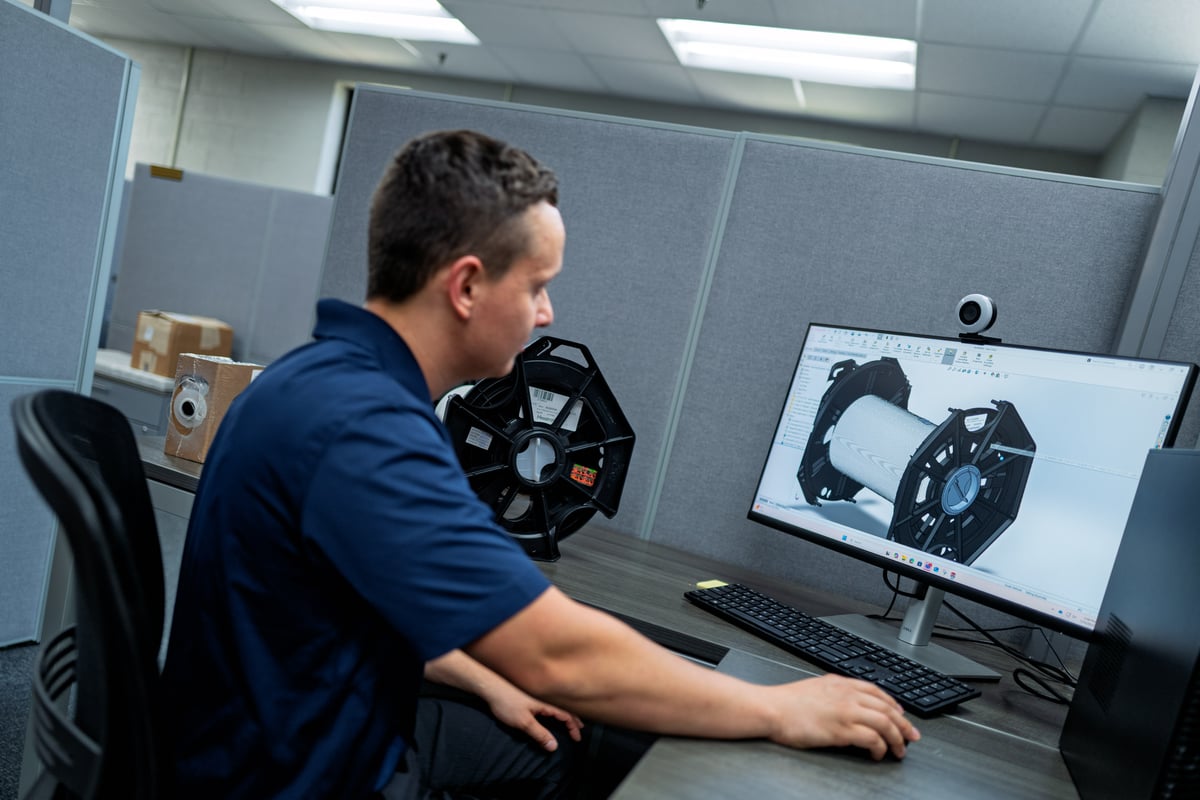 Person designing a product in 3D software at office workstation.