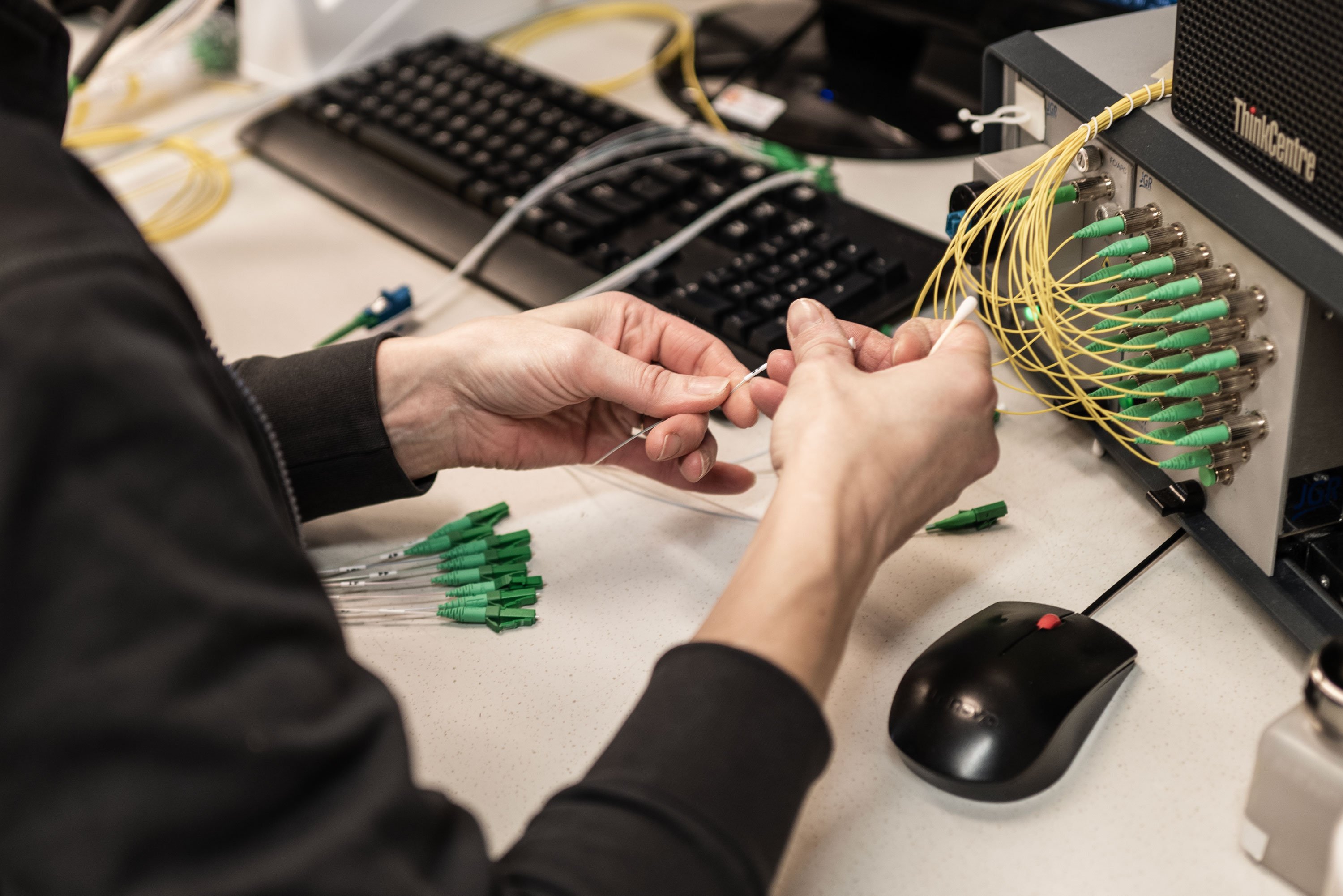 A person connecting yellow fiber optic cables to a panel. The panel is part of a computer or server system.