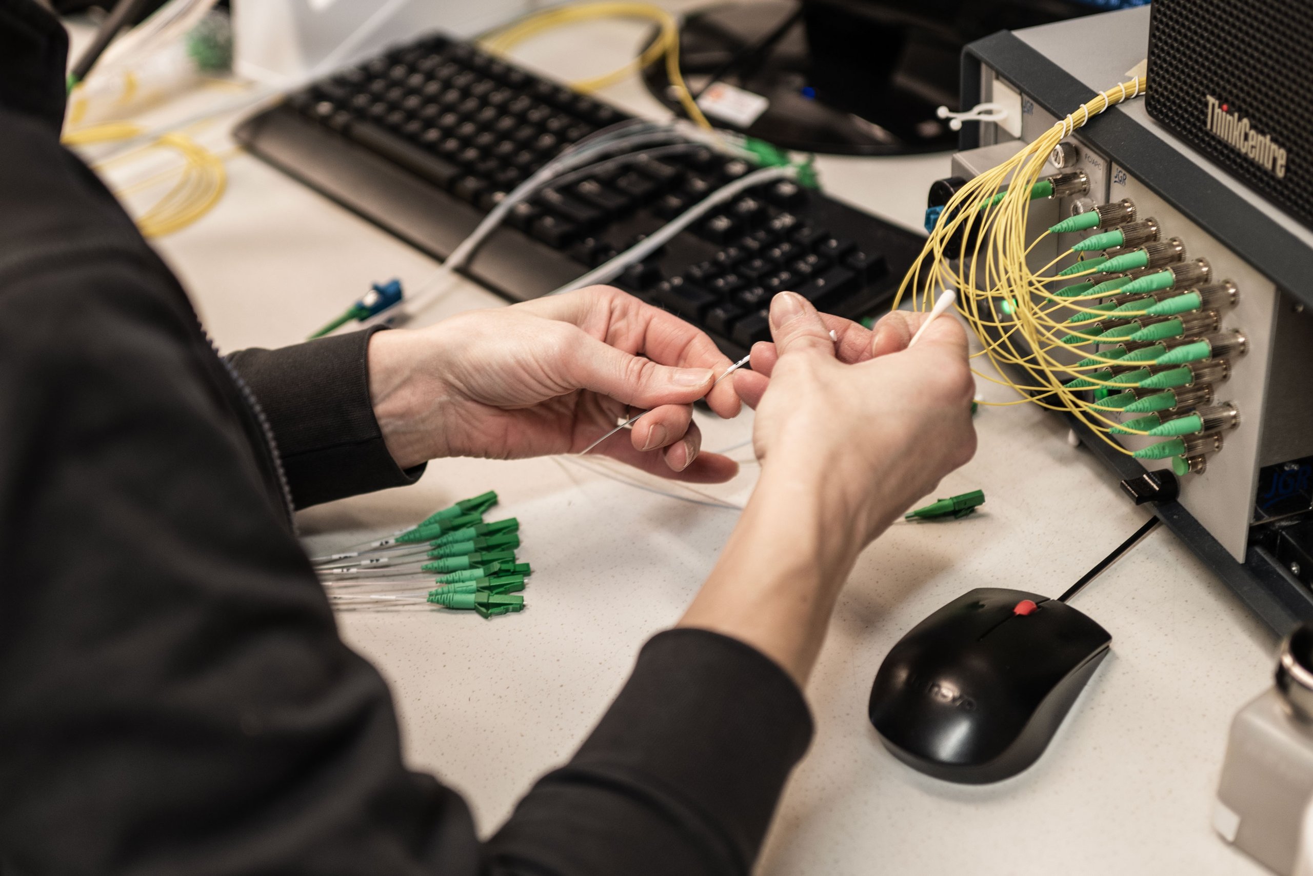 A person connecting yellow fiber optic cables to a panel. The panel is part of a computer or server system.