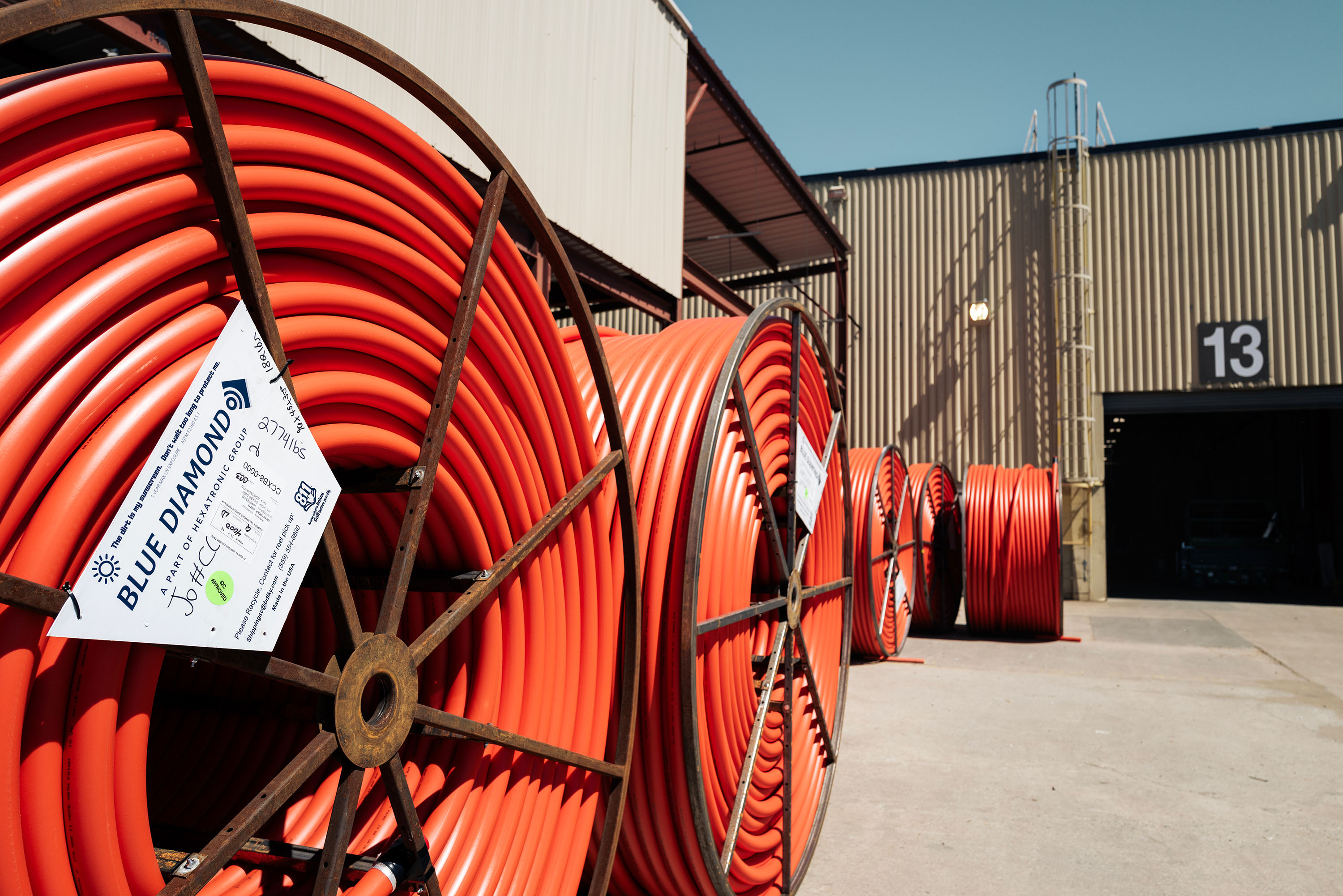 Large reels of bright orange duct are neatly coiled and stored outside a warehouse under a clear sky.
