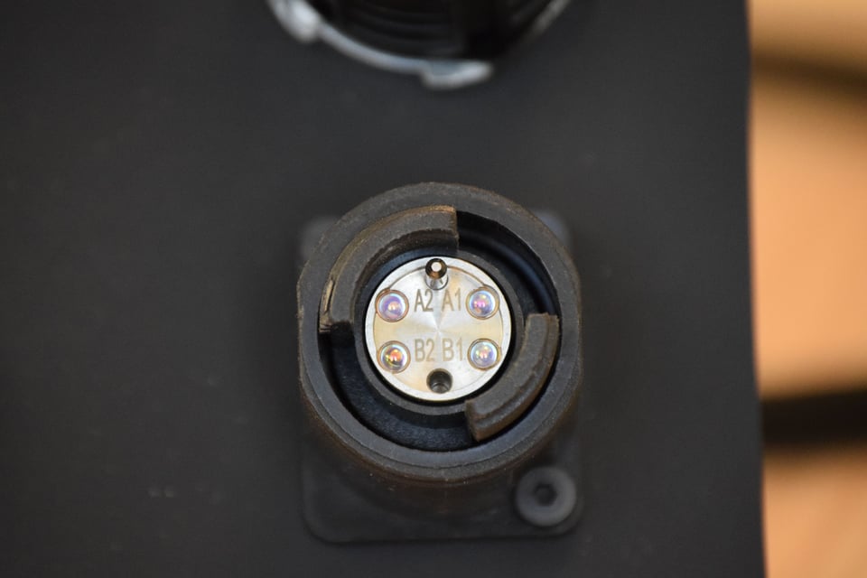 Close-up of an expanded beam connector on a black surface.