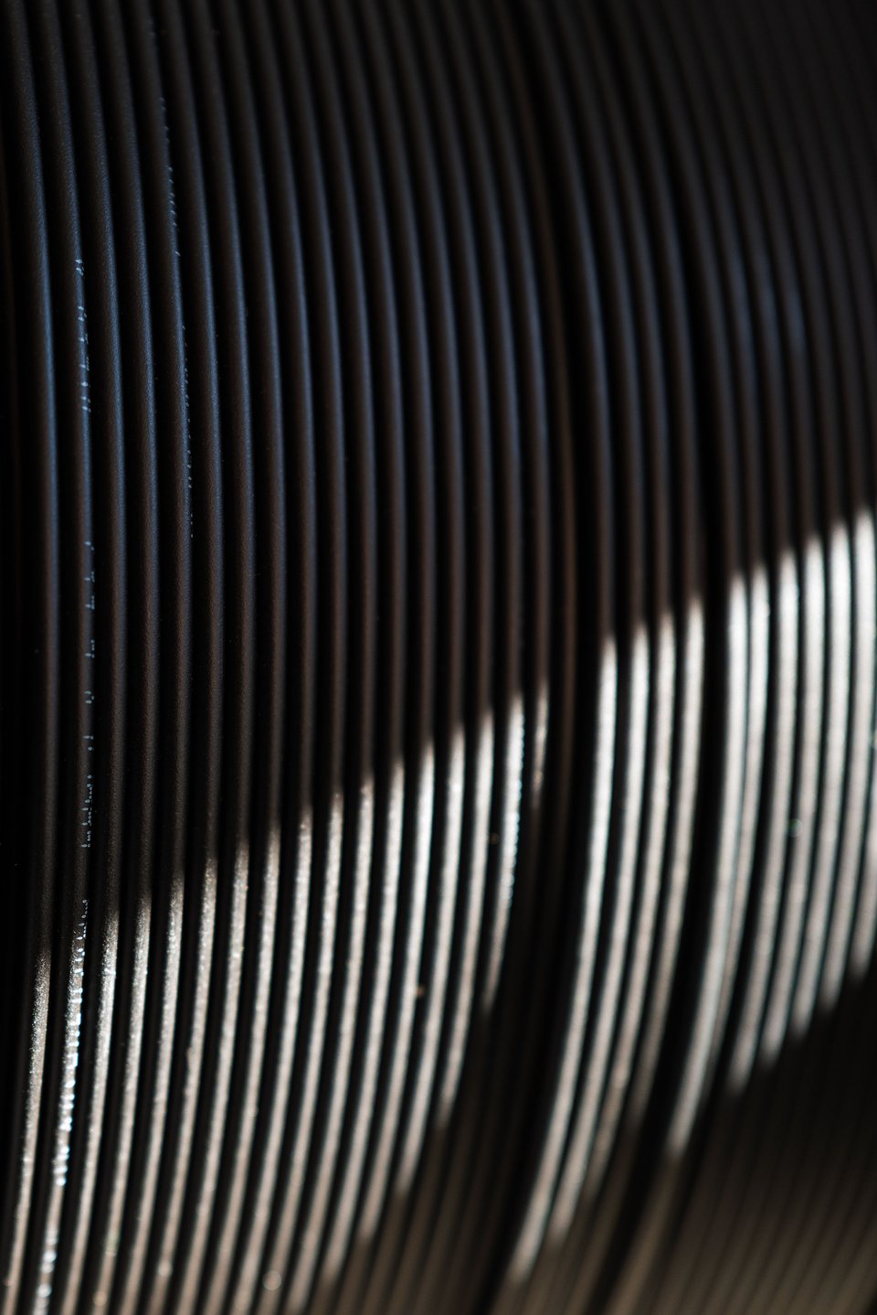 Close-up of a cable drum with black fiber cable with light reflecting off edges, creating a rhythmic, textured pattern.