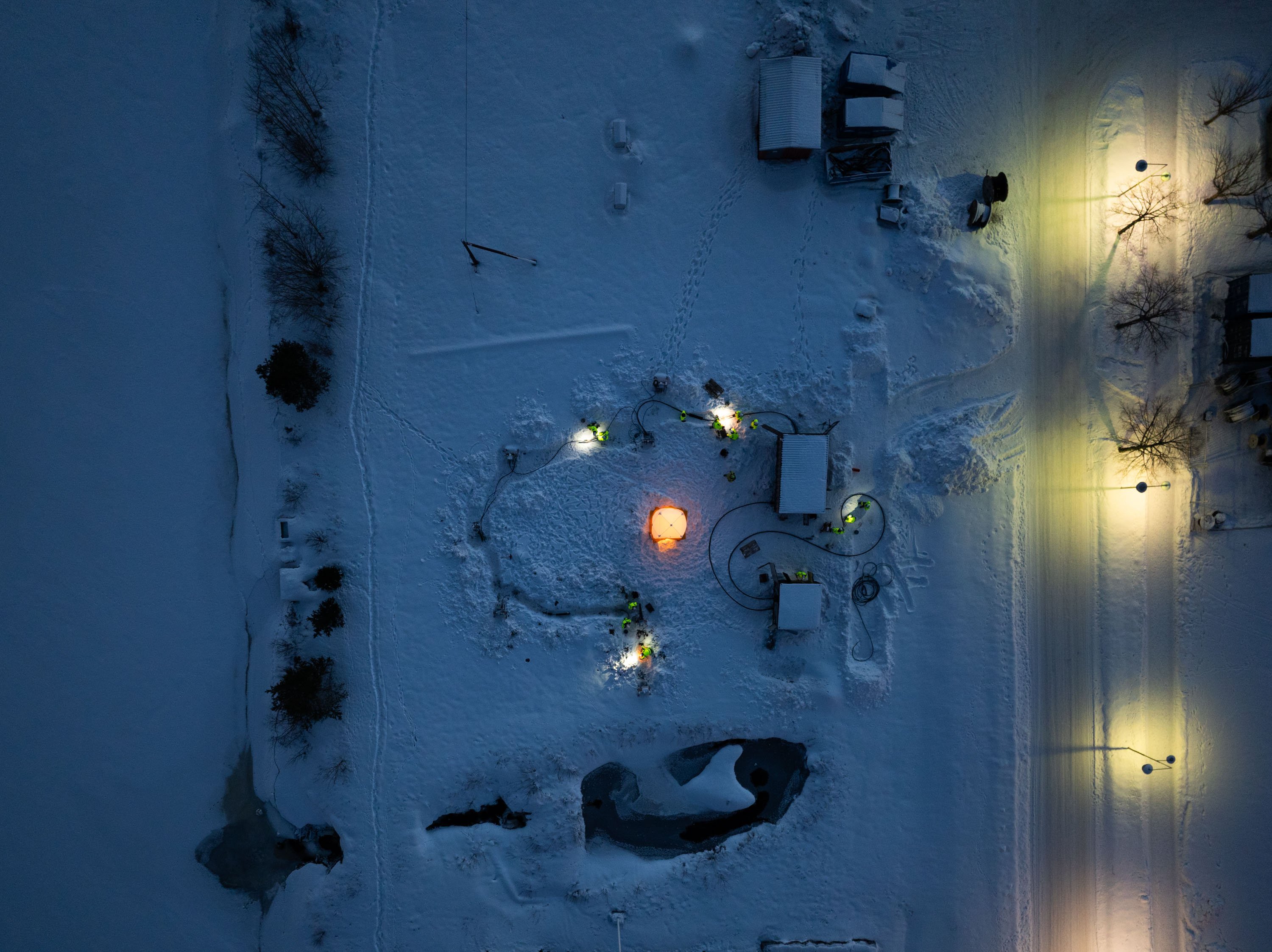Aerial view of electrical cable installation in a snow-covered field at night.