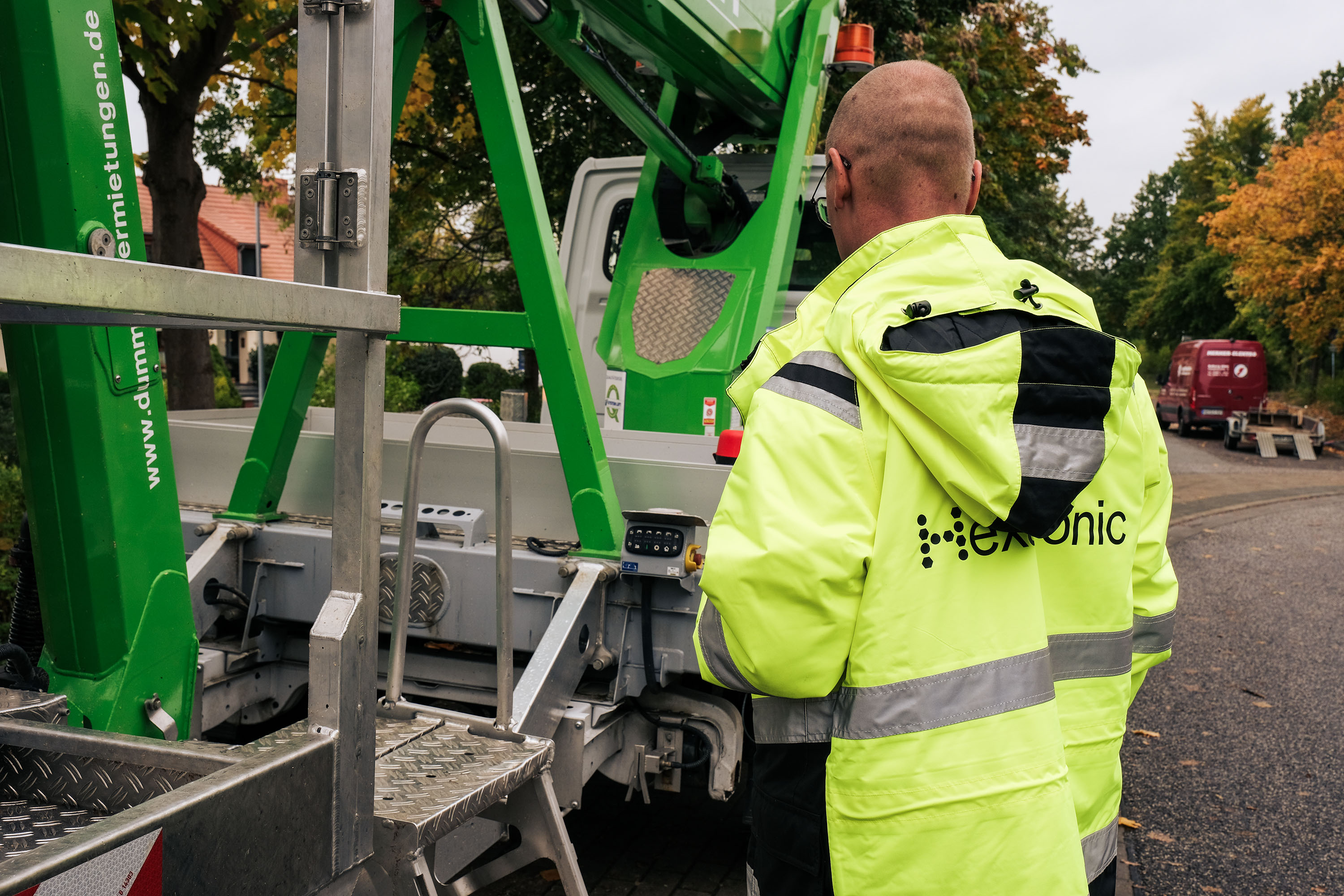 A person in a Hexatronic jacket at an outdoor construction site on a suburb street under cloudy skies.