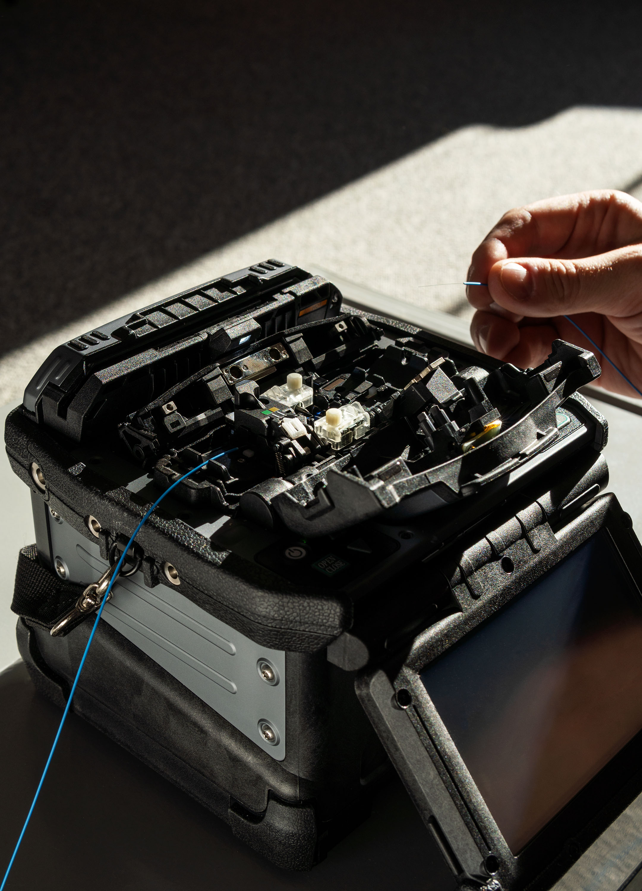 A person uses a fiber splicer. The scene is bathed in sunlight.