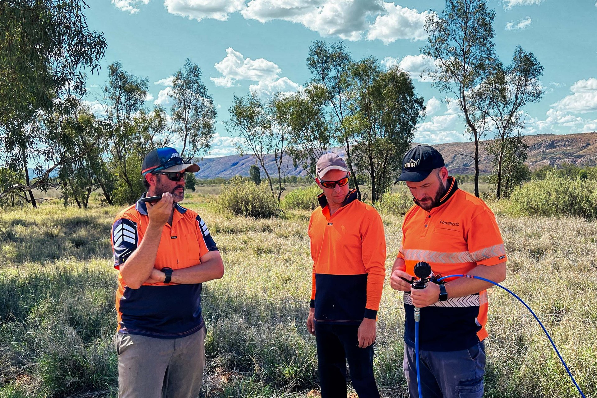 Three people in orange work clothes stand in a field and work with an installation tool with microducts attached to it.