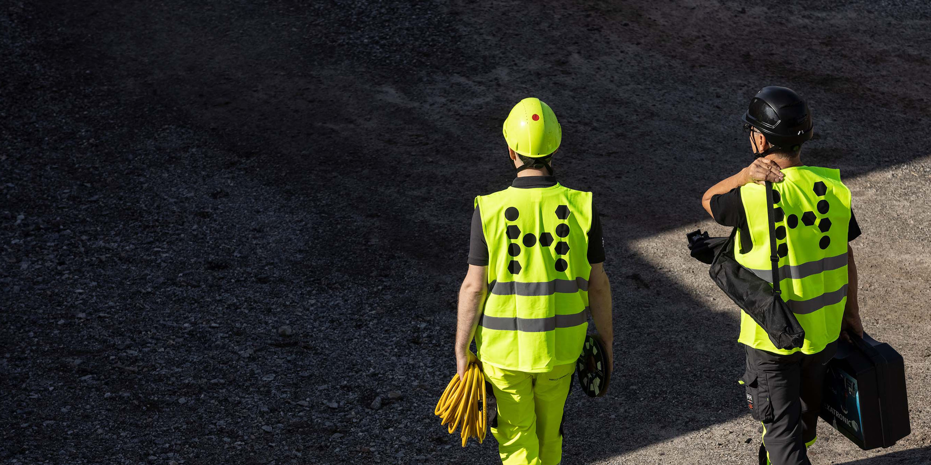 Two workers in safety vests at a construction site, surrounded by materials, indicating ongoing work.