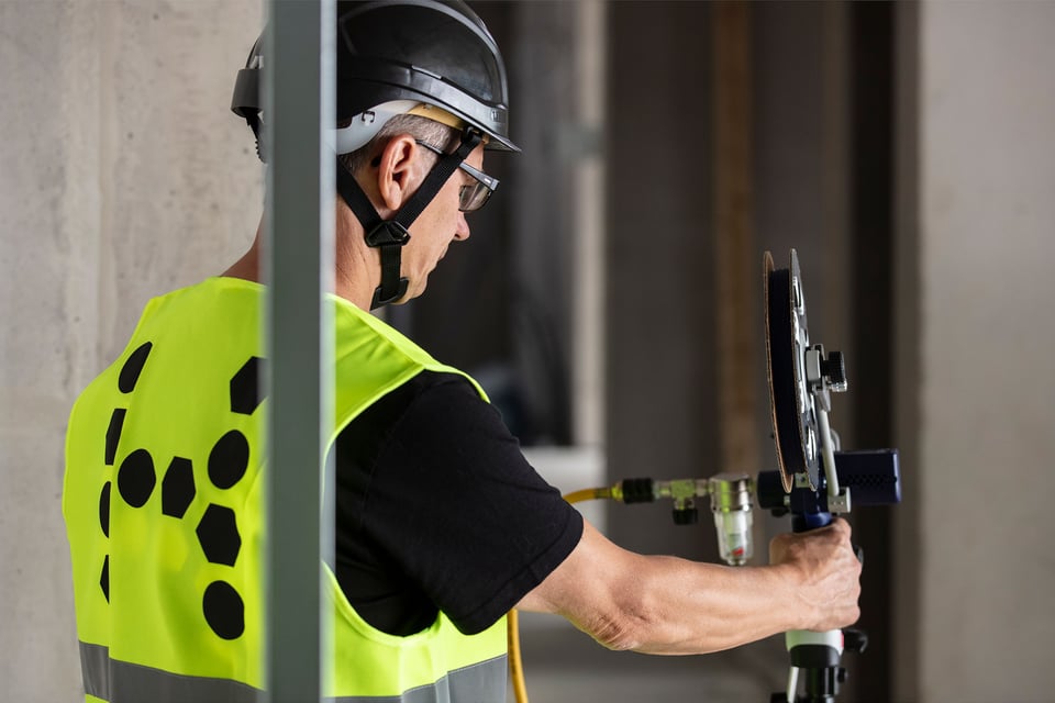 A person in safety gear is using a hand tool, likely for installing optical fiber at an indoor construction site.