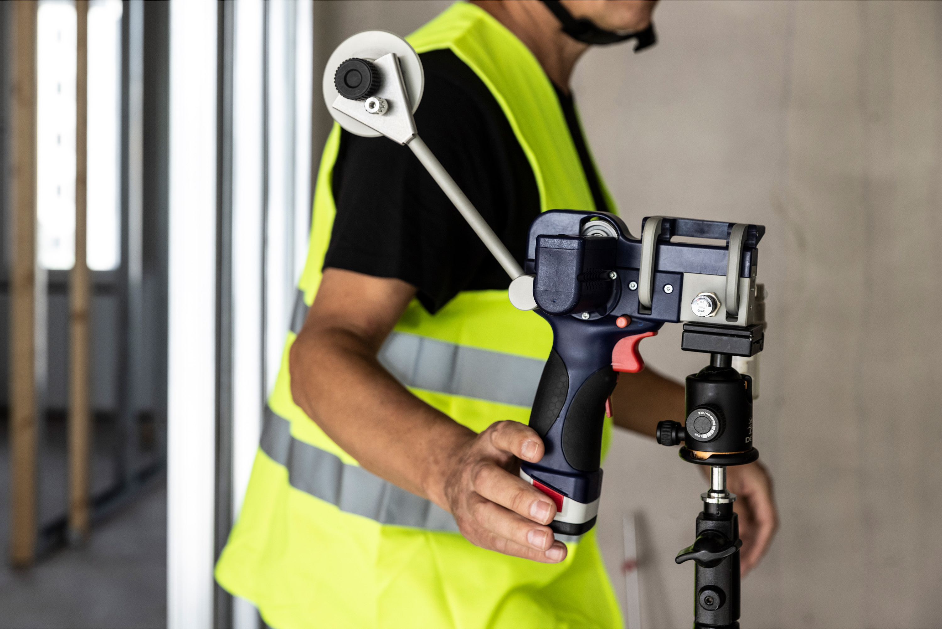 A person in a safety vest holds a Air Blown Fiber Installation Tool, ready to install optical fiber in an indoor construction area.