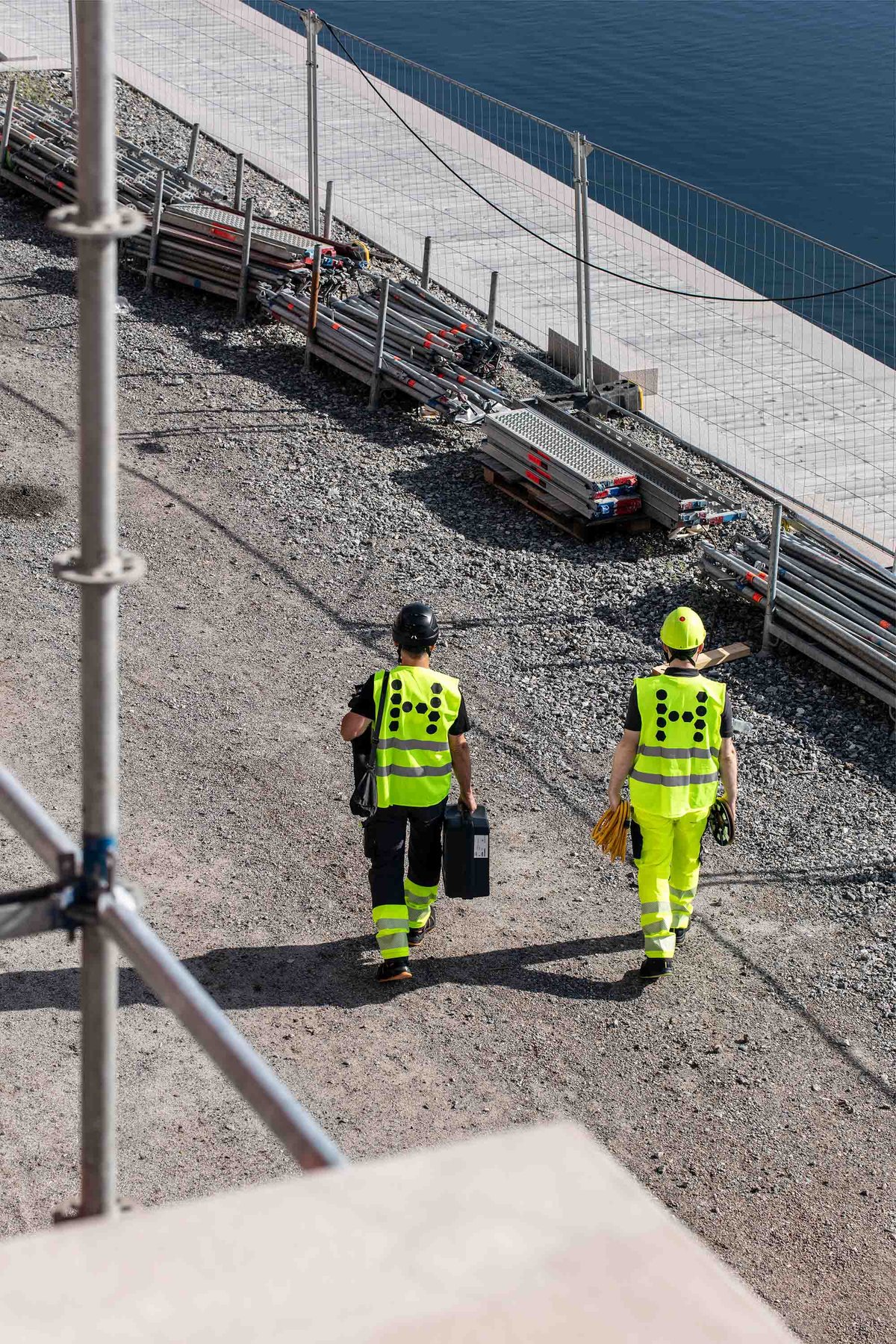 Two workers in safety vests at a construction site, surrounded by materials, indicating ongoing work.