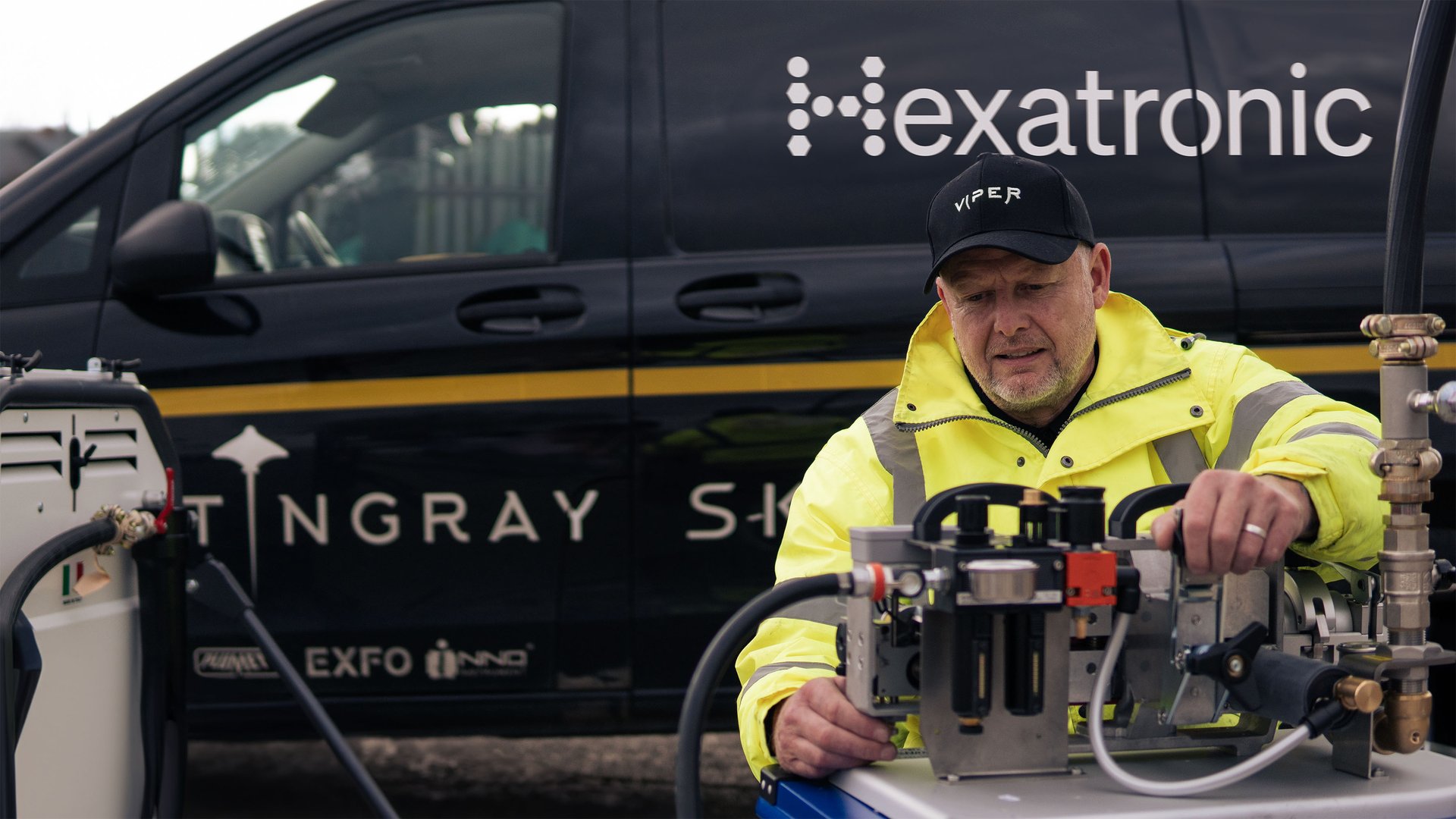 A person in a high-visibility jacket is outdoors, operating a fiber optic installation tool.