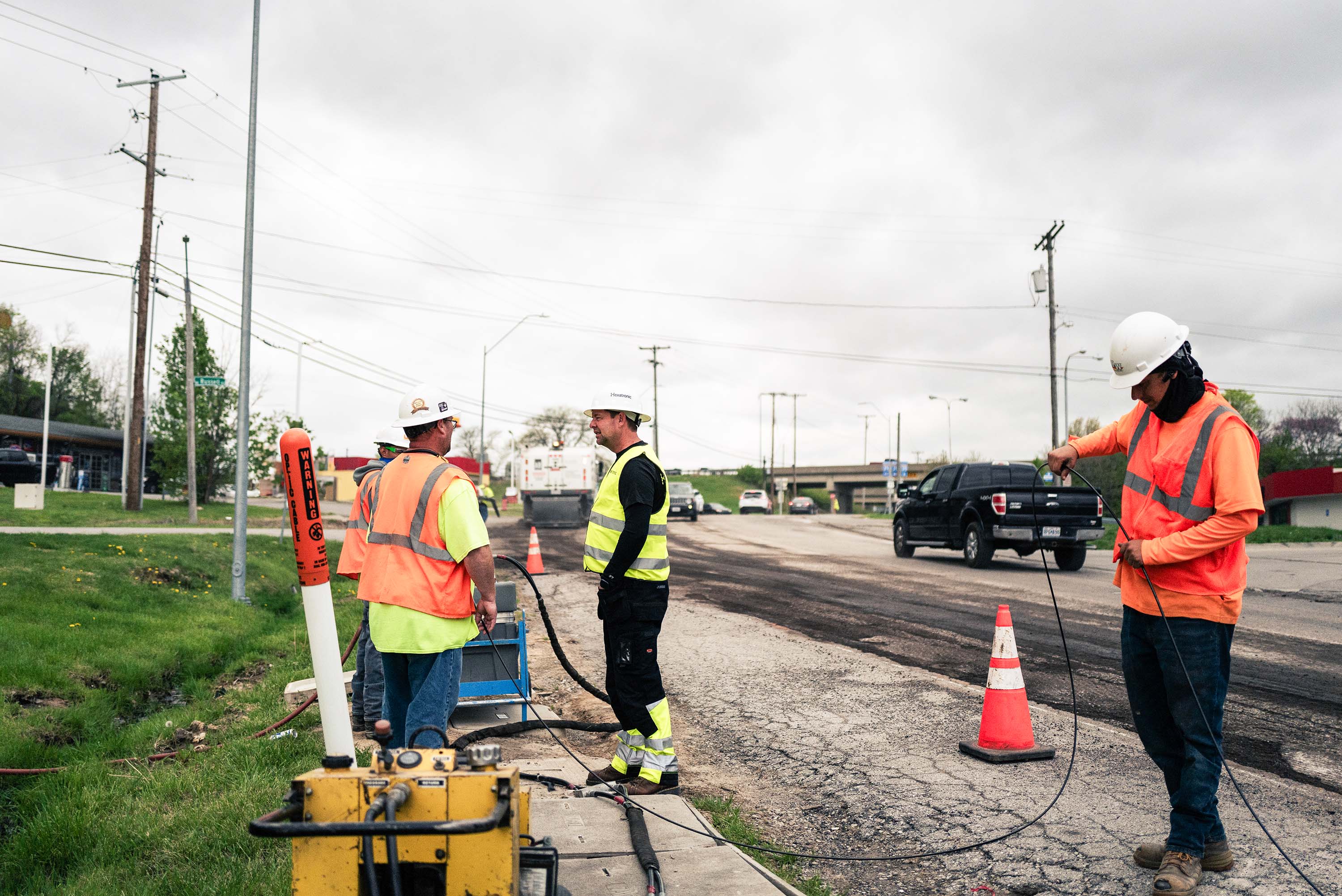 Three workers in safety gear are working on a fiber optic installation at the roadside.