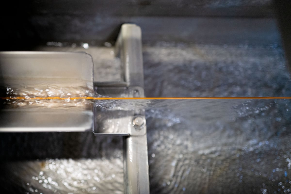 Orange fiber optic cable cooled through water in industrial setup.