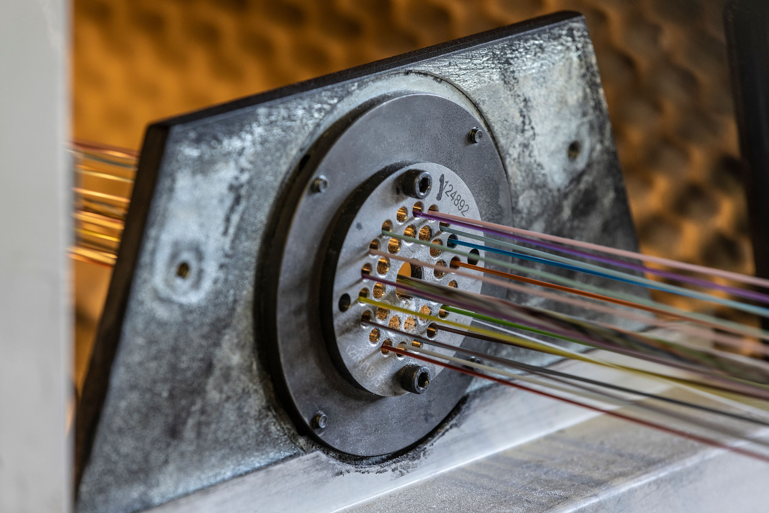 Fiber strands of different colors are braided into a cable in an industrial setting.