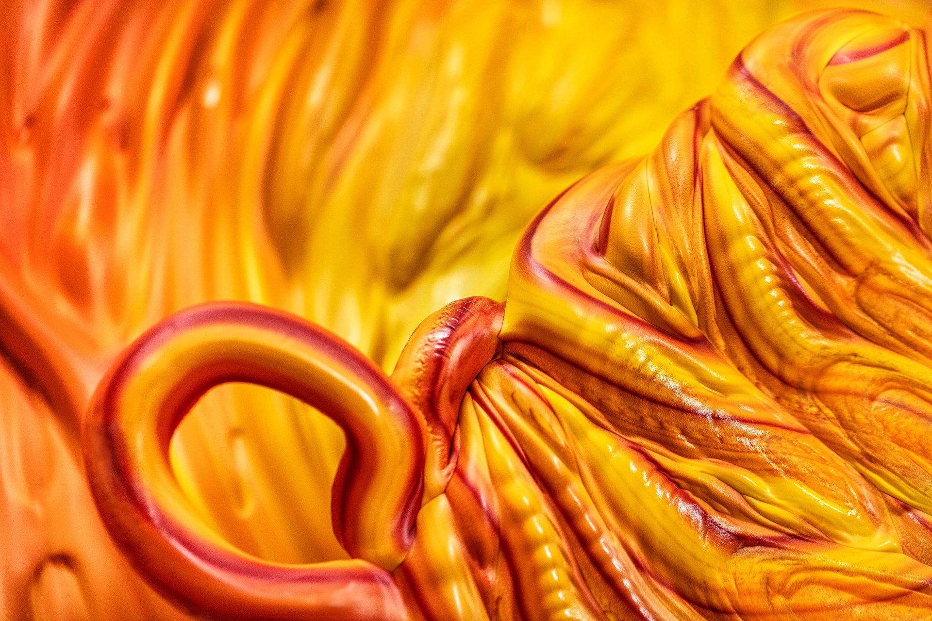 A close-up of a vibrant, textured surface with swirling patterns in warm yellow and orange hues, resembling a fluid or organic shape.