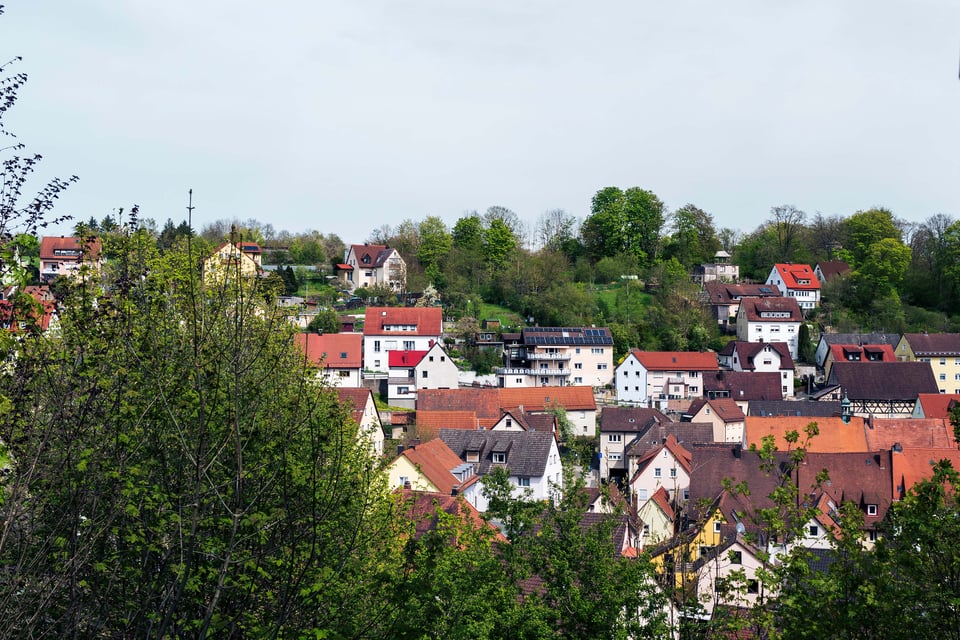 A scenic village with colorful houses nestled among lush green trees, under a bright, cloudy sky.