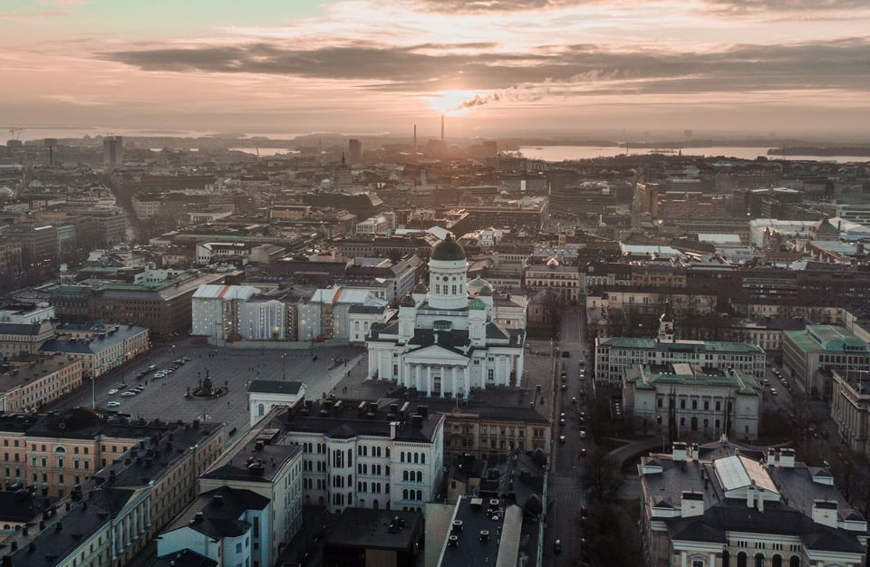 A cityscape at dawn, grand cathedral prominent, buildings in soft light, calm streets, sun rises over distant waters.