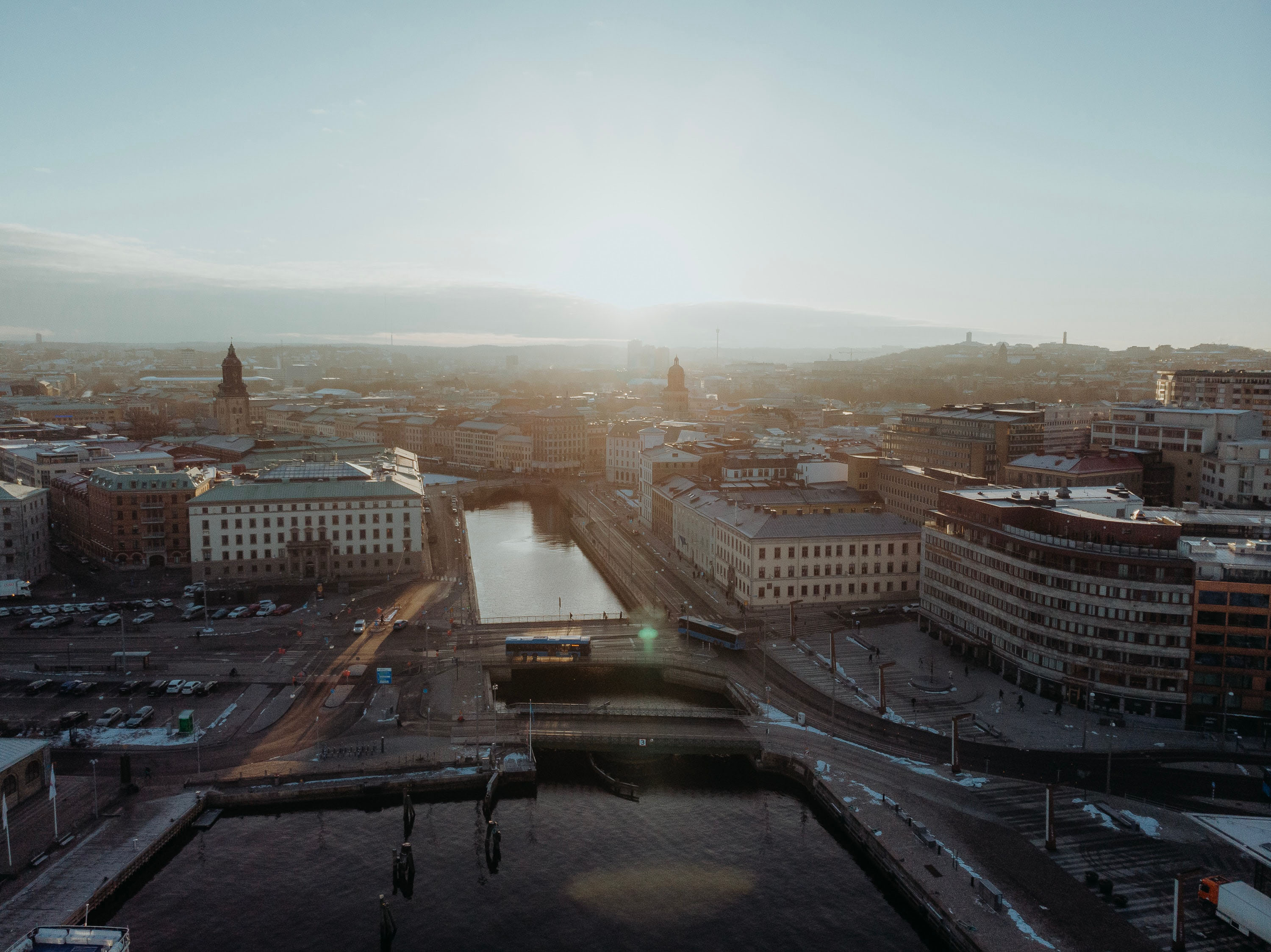 Sunrise over a city with varied buildings, a river reflects the light. A serene, peaceful atmosphere prevails.