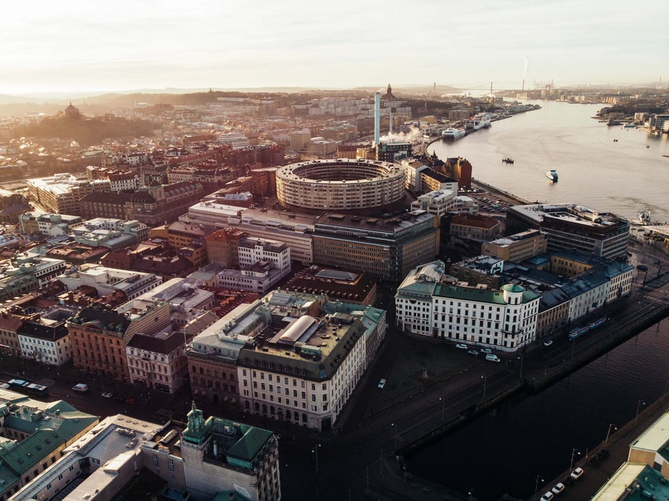 Aerial view of a city with diverse architecture, a circular building, river, bridges, under the warm glow of the setting or rising sun.