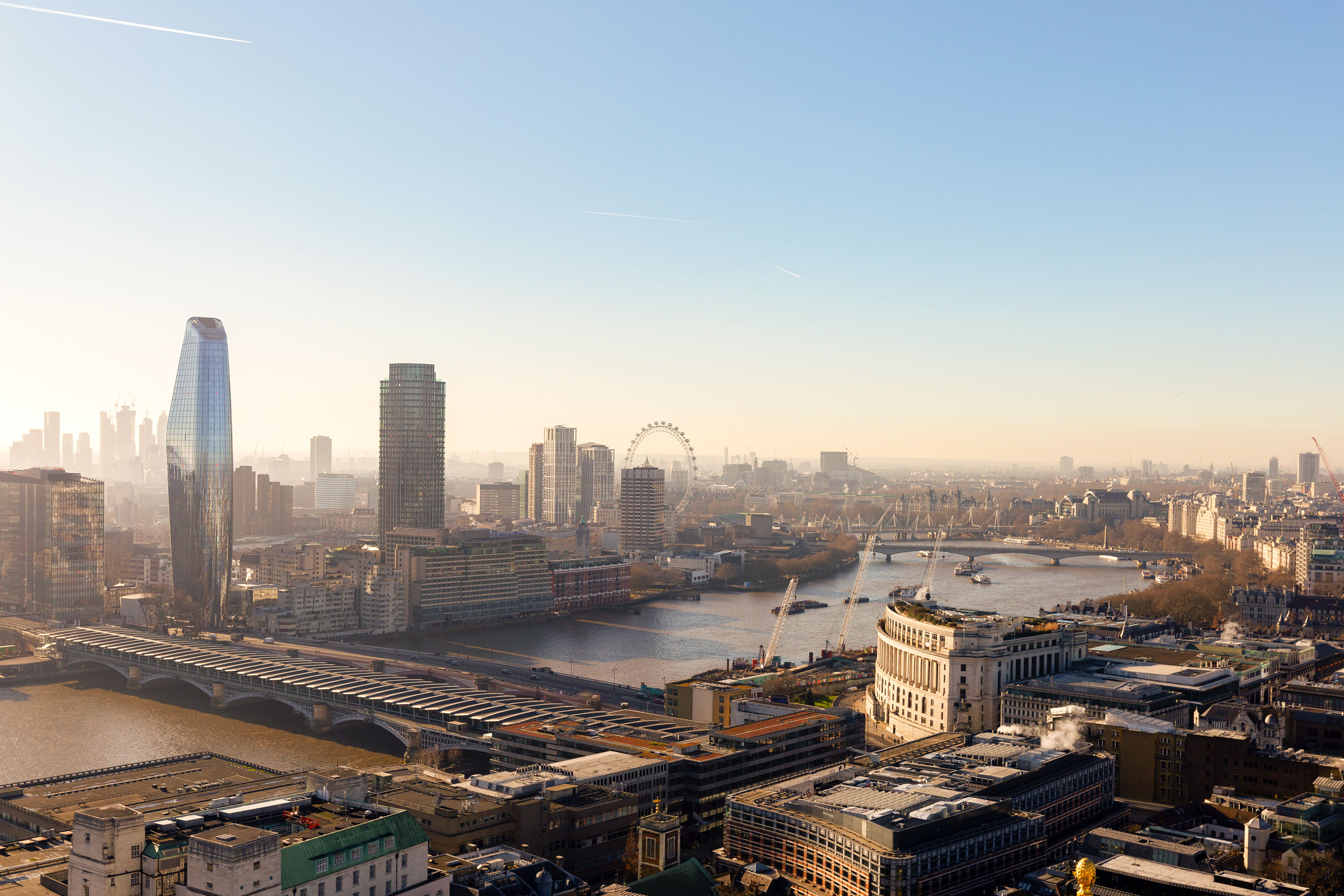 Daytime panoramic view of London with skyscrapers, the London Eye, bridges over the Thames River, under a clear sky.