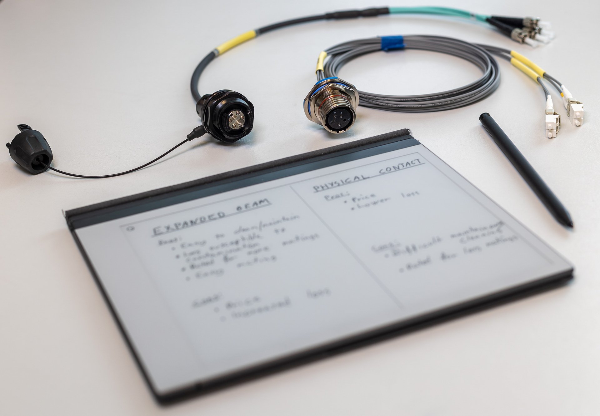 A touchpad with a comparison of expanded beam and physical contacts. Expanded beam connectors and a pen is laying on the white table too. 