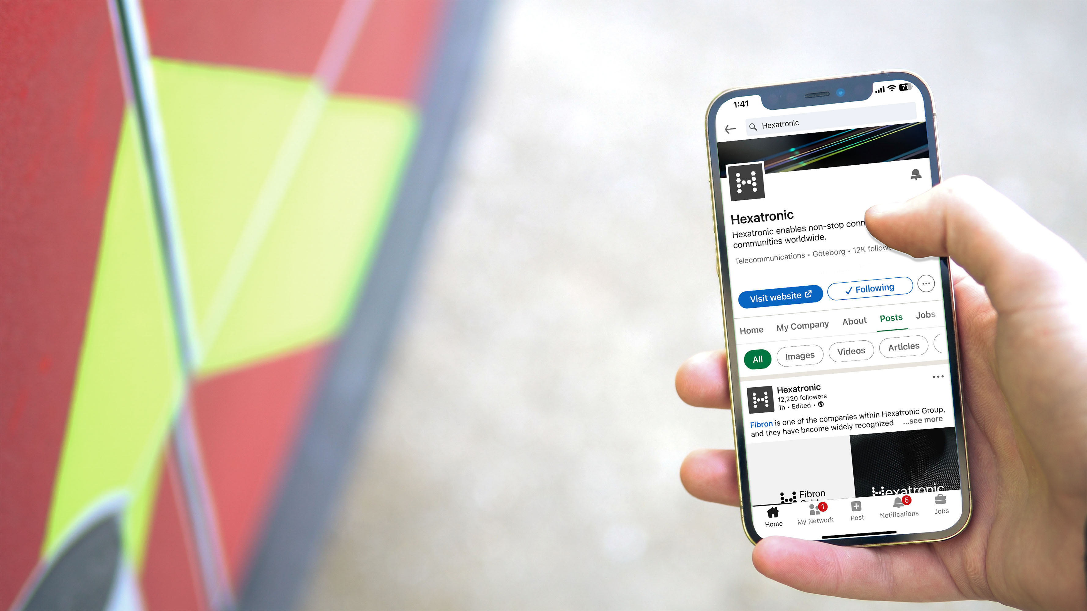 A person scrolls on a smartphone. The screen shows Hexatronic's Linkedin account.