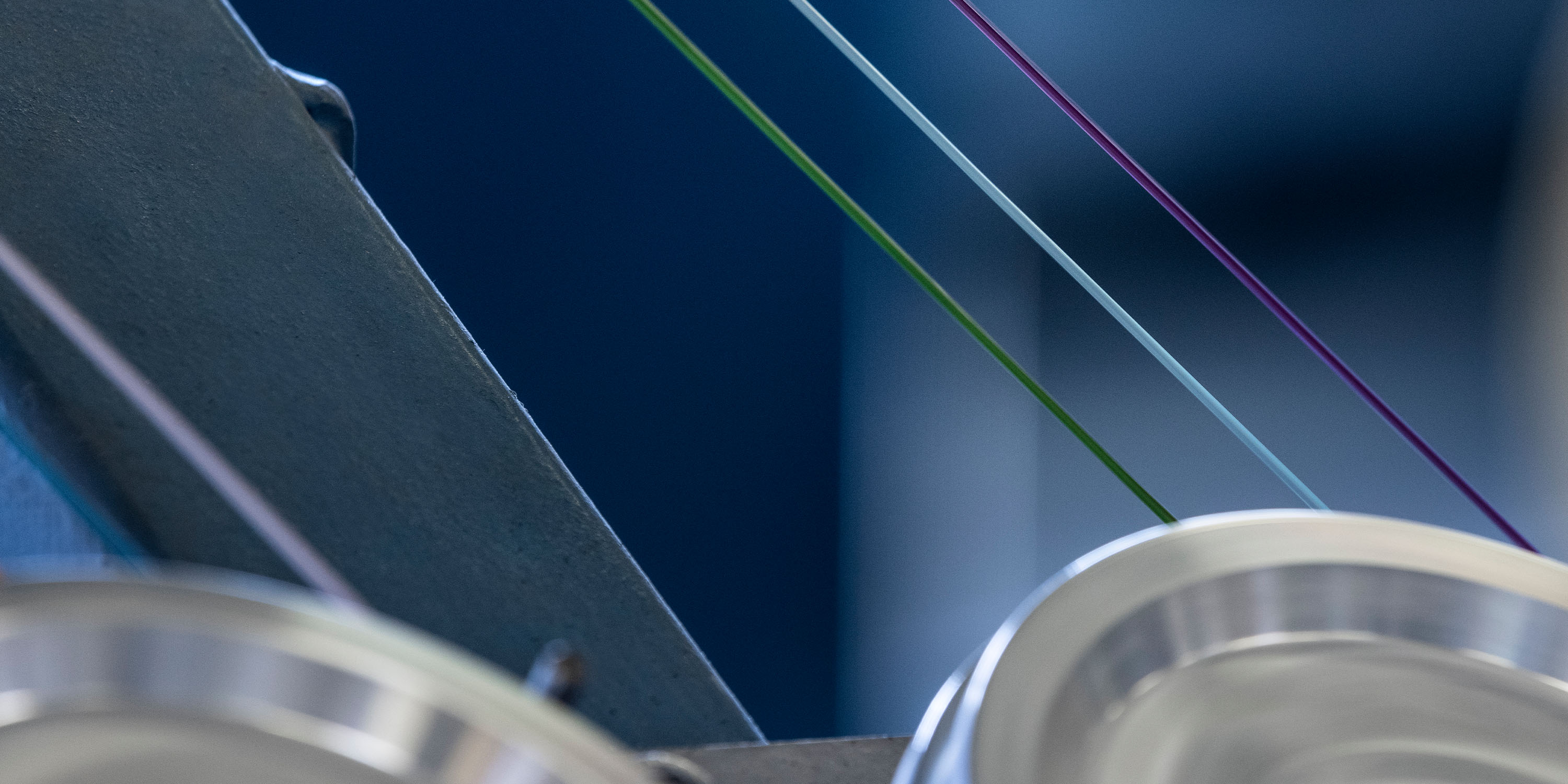 Close-up of industrial machinery with colorful fiber optic threads running over spinning wheels, likely for cable manufacturing.
